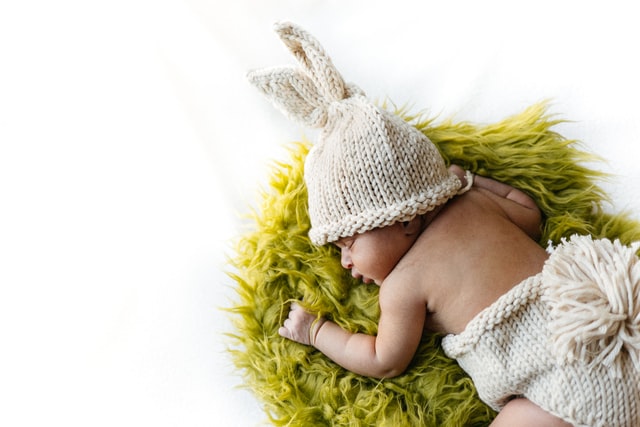 Used baby clothes-Baby laying on a green rug in a cute knitted outfit