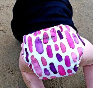 Pea Pod Cloth Nappies-Baby crawling on the beach wearing a purple pea pod nappy