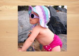 Cancer Council sunglasses review 2020-Baby standing by rocks wearing Cancer Council Sunglasses and a sunhat