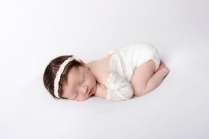 5 benefits organic baby clothes have-baby laying down in white baby suit and hairband.