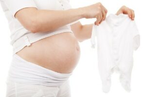 Would you consider renting the baby clothes for a newborn baby?-Pregnant lady holding a white baby suit.