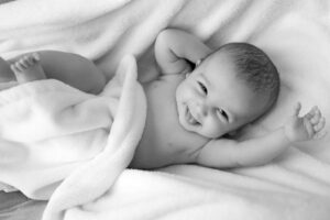 Best baby clothes for newborn babies with a sensitive skin-Smiling baby laying in blankets with the hands next to the face.