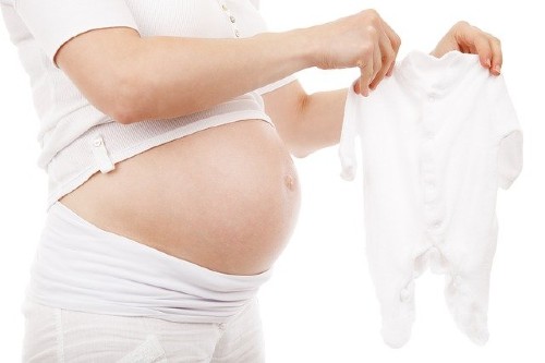 Would you consider renting the baby clothes for a newborn baby?- Pregnant lady holding a white bodysuit.