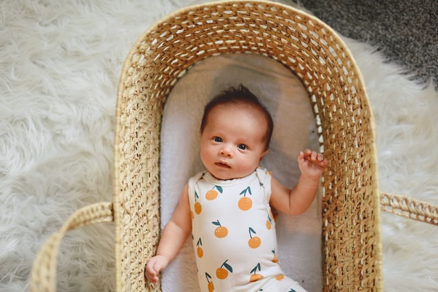 Trendy baby clothes for boys-Baby in crib wearing a bodysuit with orange print.