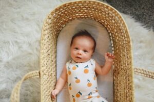 Trendy baby clothes for boys-Newborn baby in crib wearing a bodysuit with oranges.