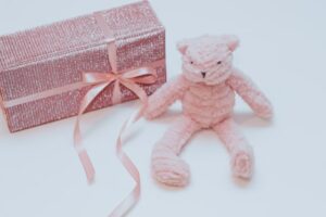 What's the best baby shower gifts?-Nice wrapped gift with pink ribbon and soft toy sitting next to the pressie.