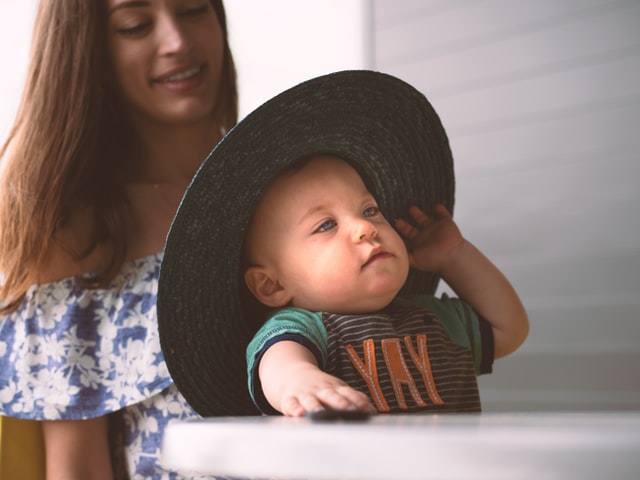 Trends in baby clothes for boys-Baby bioy wearing green shirt with letter print and broad brimmed sun hat.