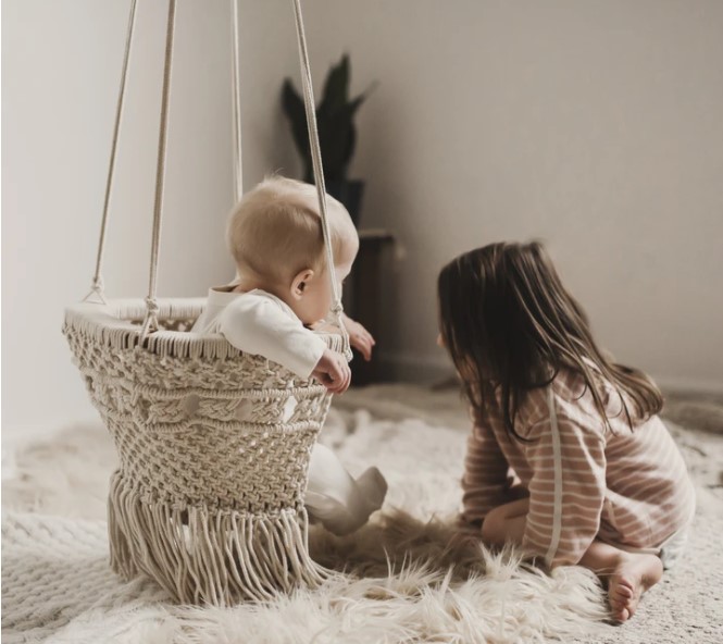 Organic cotton baby's swings-Baby in macramé baby swing with older child on a rug on the side.