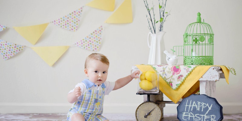 What is a Baby Bunting?-A baby sitting on the floor with a yellow themed baby bunting in the background.