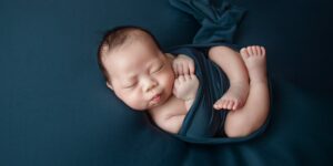 What are the most expensive baby clothes brands?-Newborn baby in wrapped in a blue colored cloth.