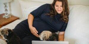 Is baby registry a thing in Australia?-Pregant lady sitting on a bed with a dog behind her laptop.