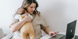 Does Amazon have the best baby gift registry in Australia?- Mother sitting behind a laptop while holding a baby.