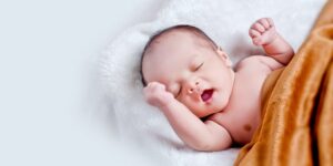 Best adaptive baby clothing Australia.- Baby laying in a bed with a blanket.